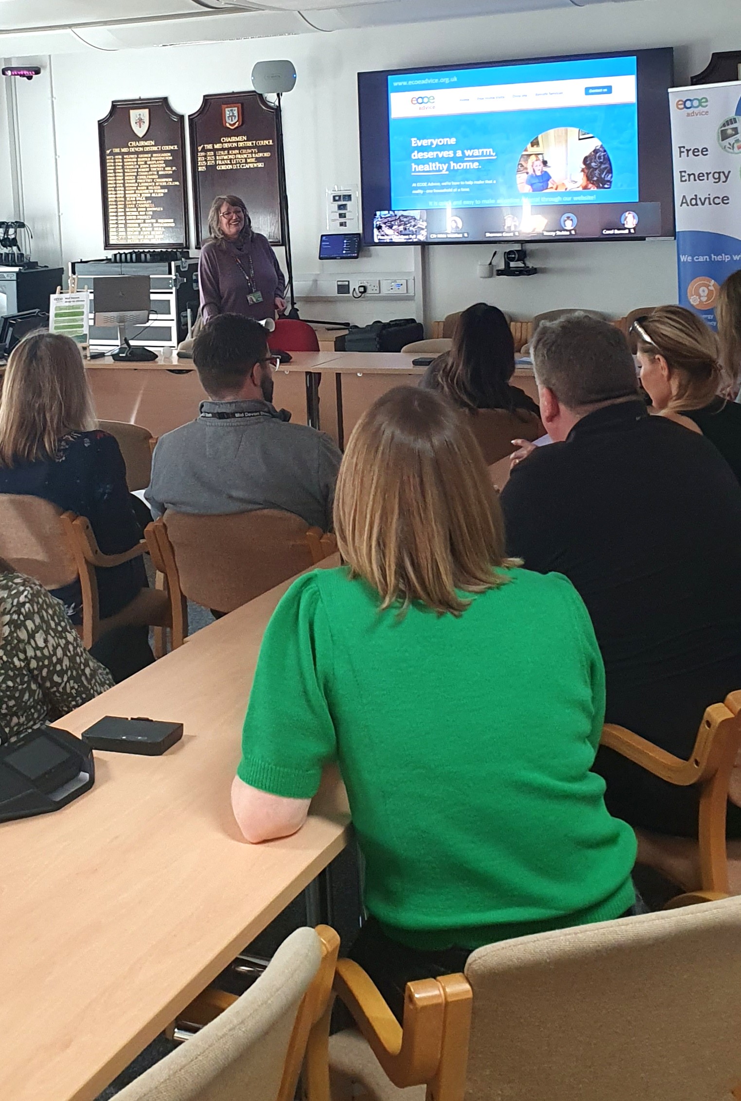 Team member giving a talk in front of a presentation screen with audience backs